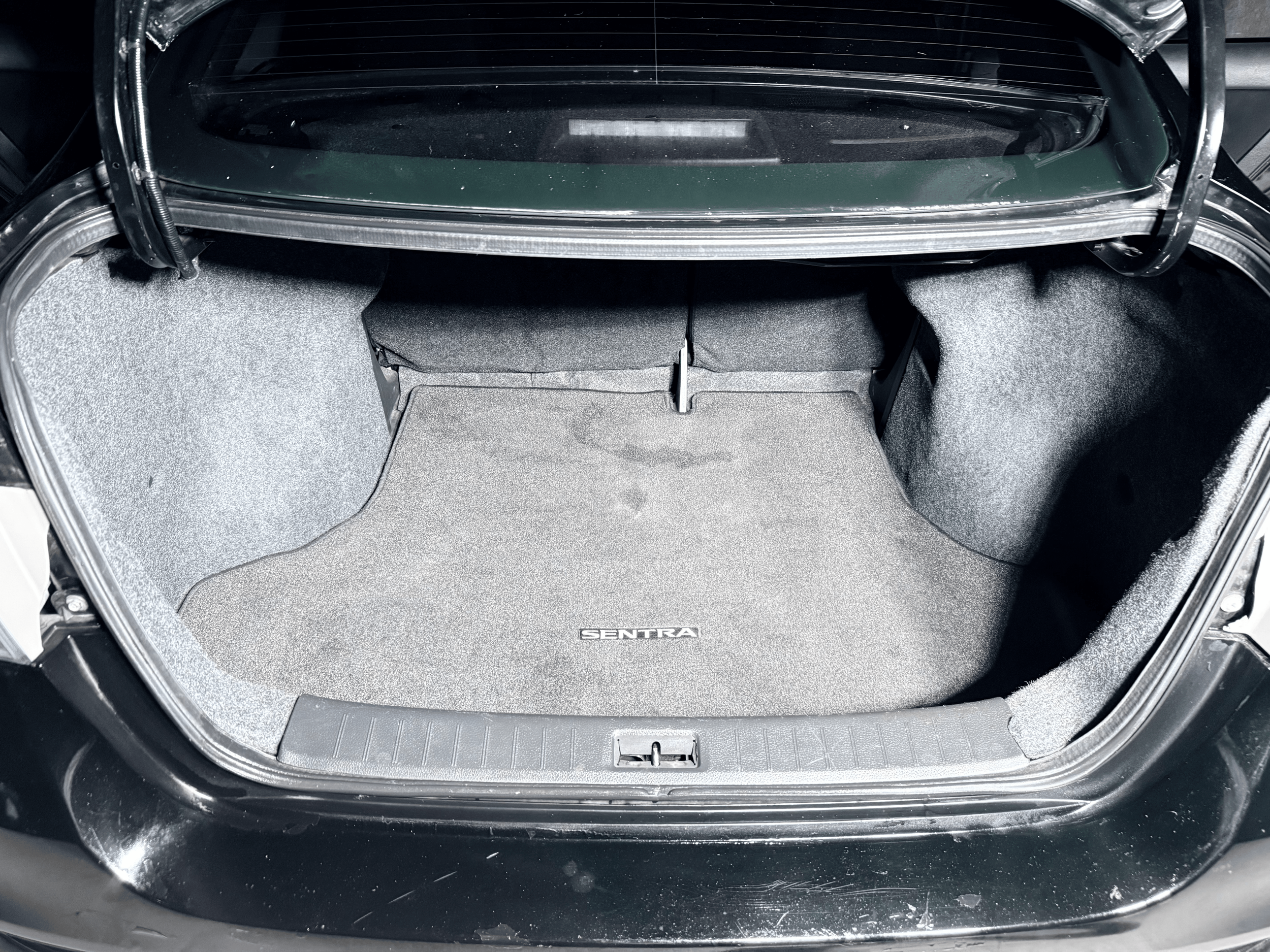 View of a car trunk showing a gray carpeted interior with the brand name SENTRA on the floor mat.