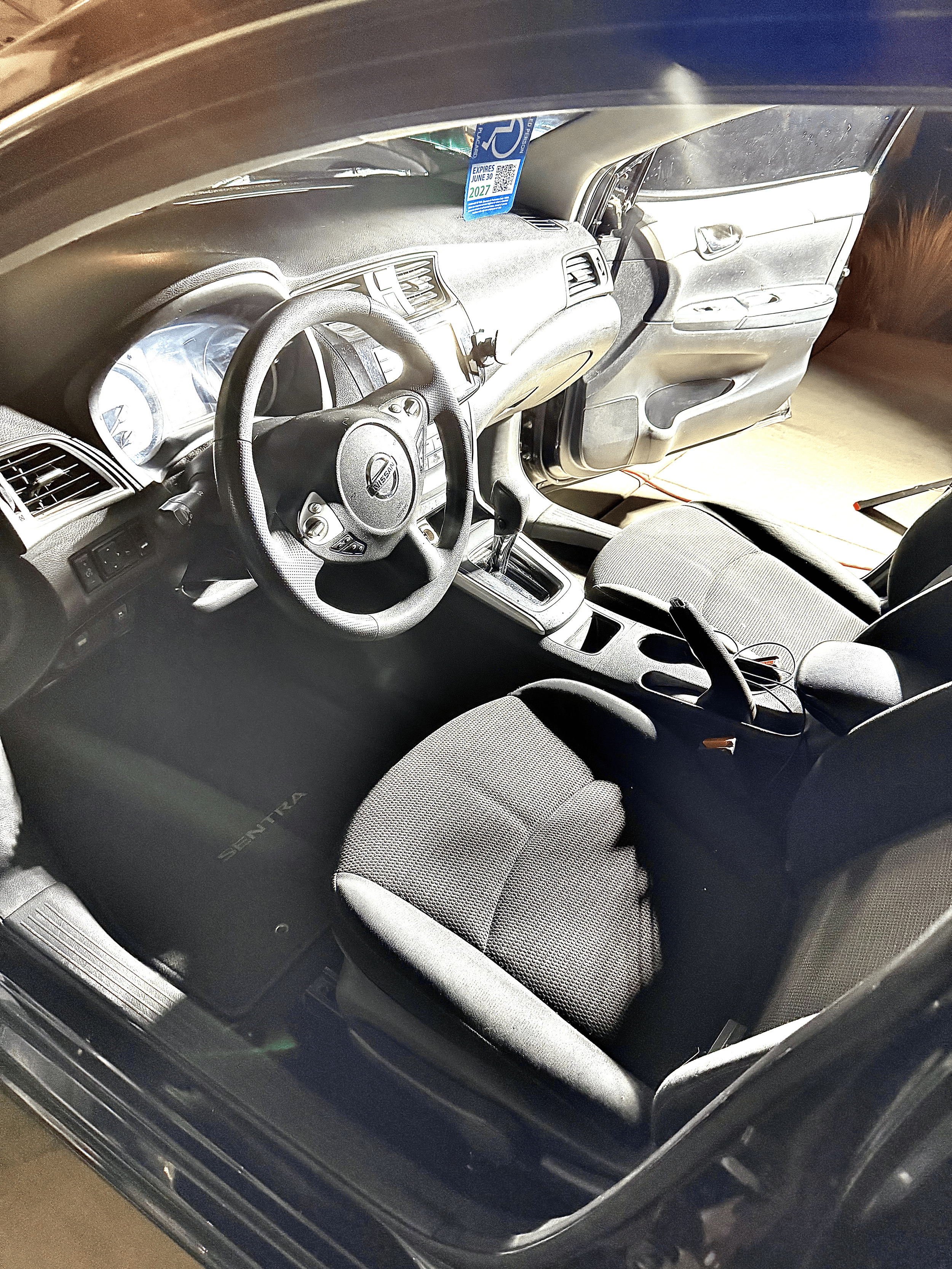 The interior of a Nissan Sentra car, showing the steering wheel, dashboard, driver and passenger seats, and the open passenger side door.
