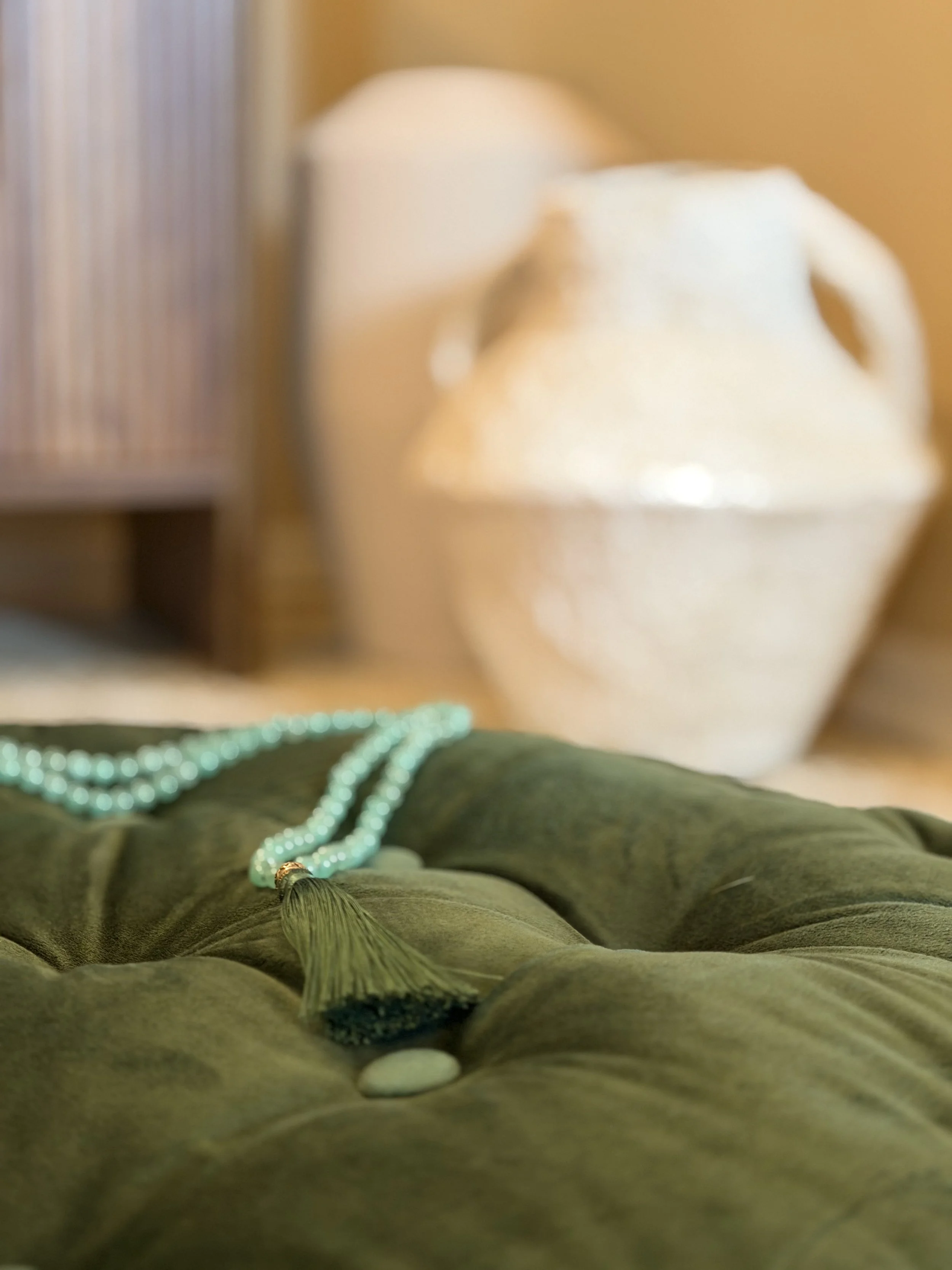 A string of light blue beads resting on a dark green tufted fabric surface. A gold and black tassel hangs from the beads.
