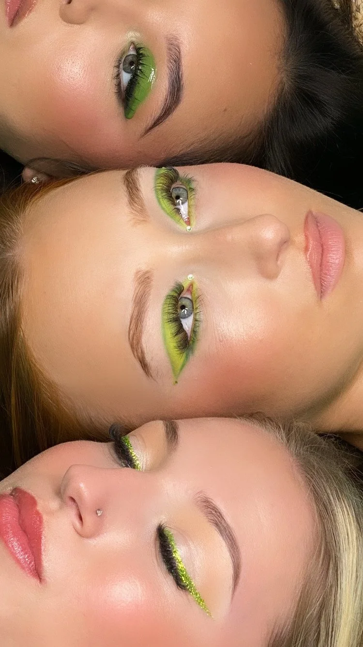 Close-up of three women lying down with their eyes closed, showcasing vibrant green eye makeup and long eyelashes. Creative makeup photoshoot.