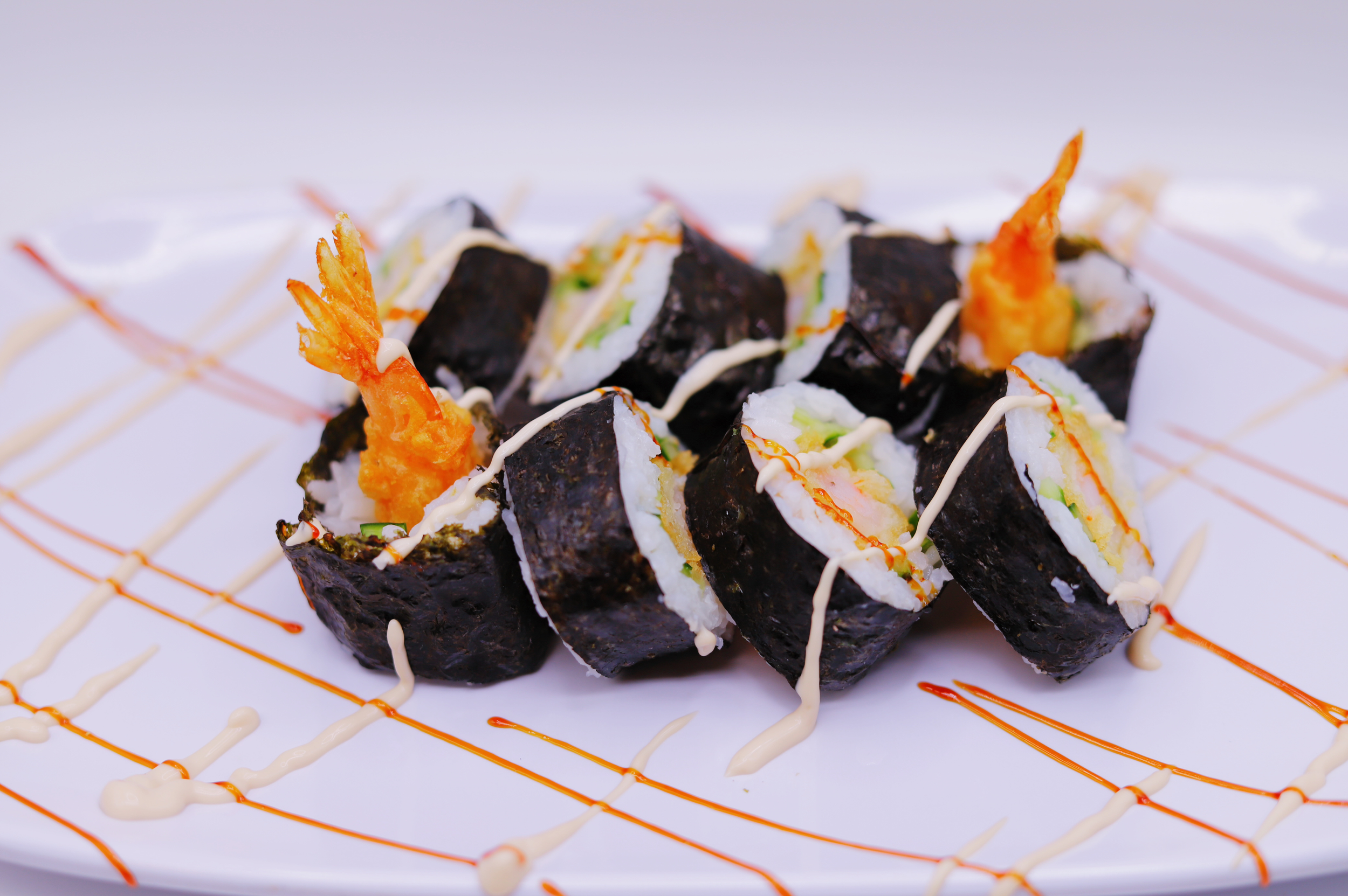Shrimp tempura roll with black nori on the outside and colorful sauce decoration on the plate