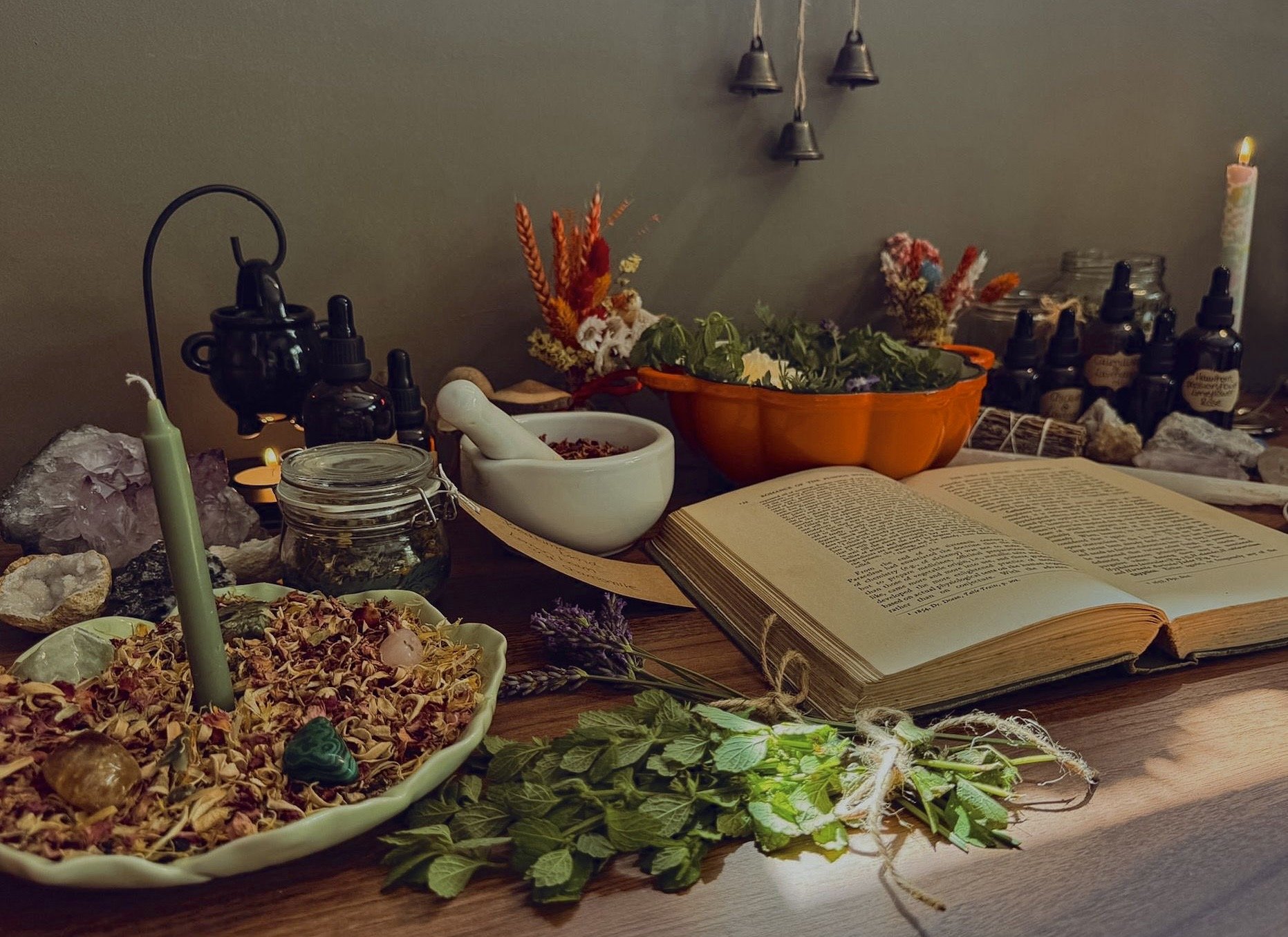 A tabletop display featuring crystals, herbs, essential oils, an open book, and various spiritual tools, including candles and small boxes.