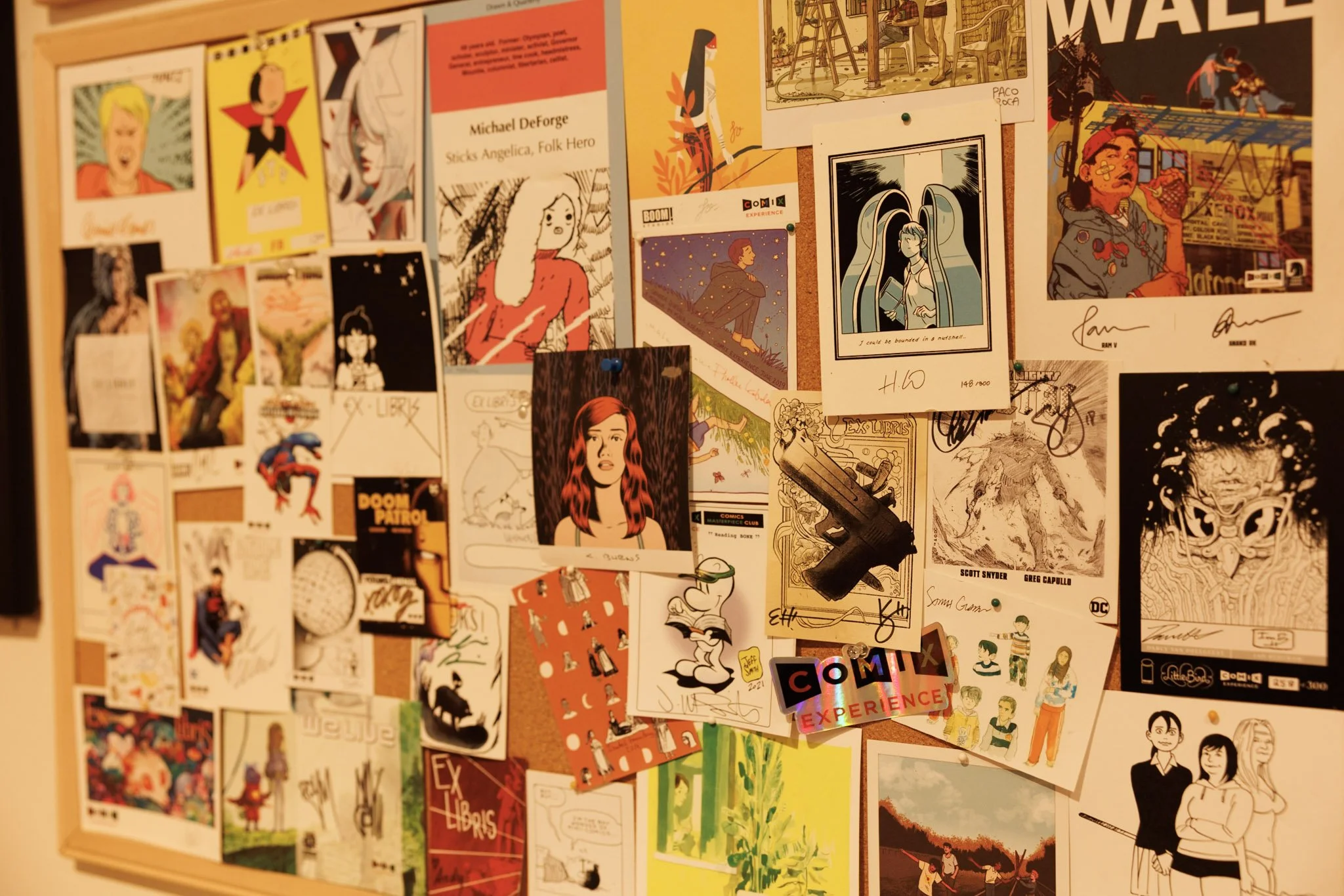 A collage of various comic book and graphic art posters pinned on a board, featuring characters, artwork, and signatures in different styles and colors.