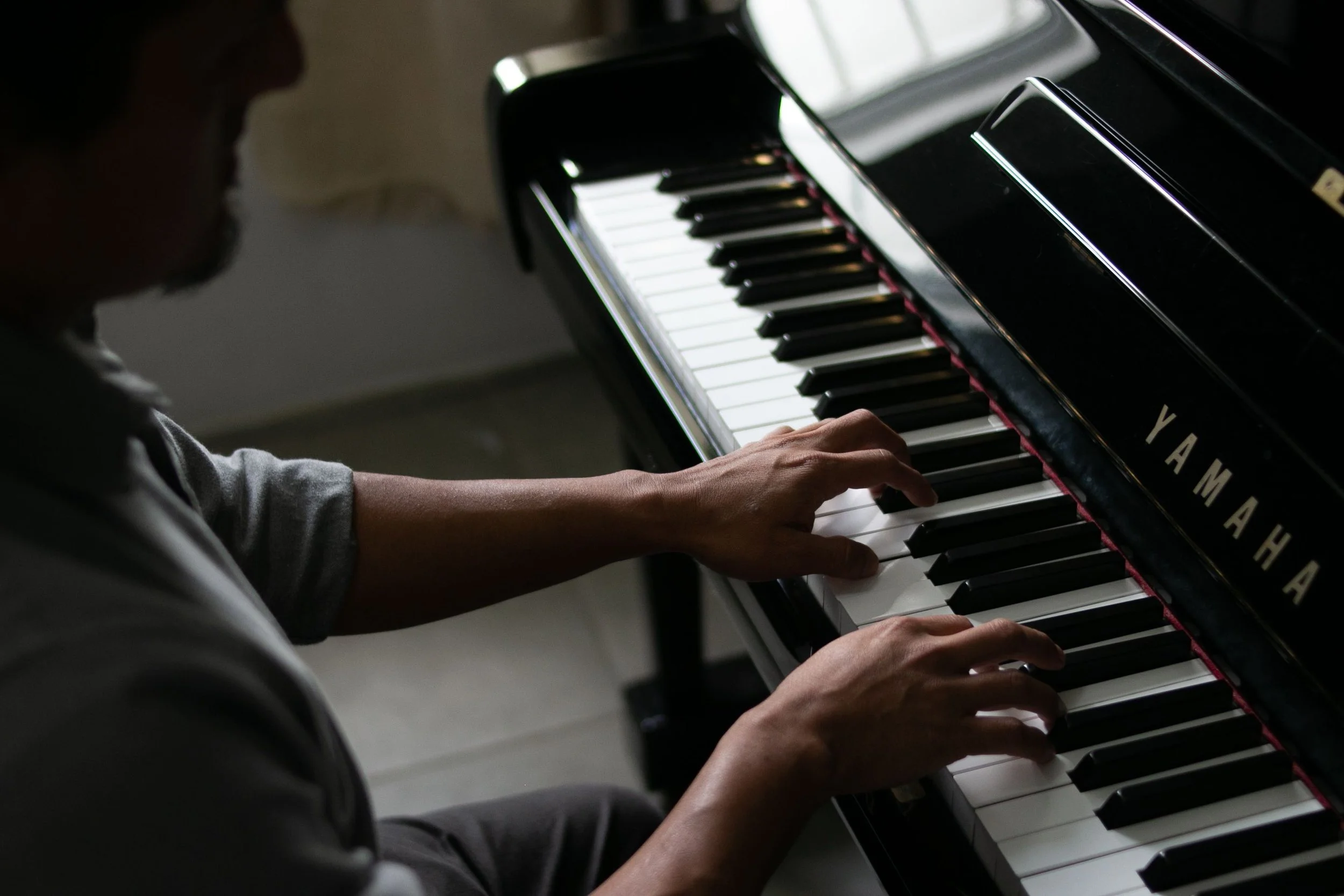 A person playing a Yamaha grand piano indoors.