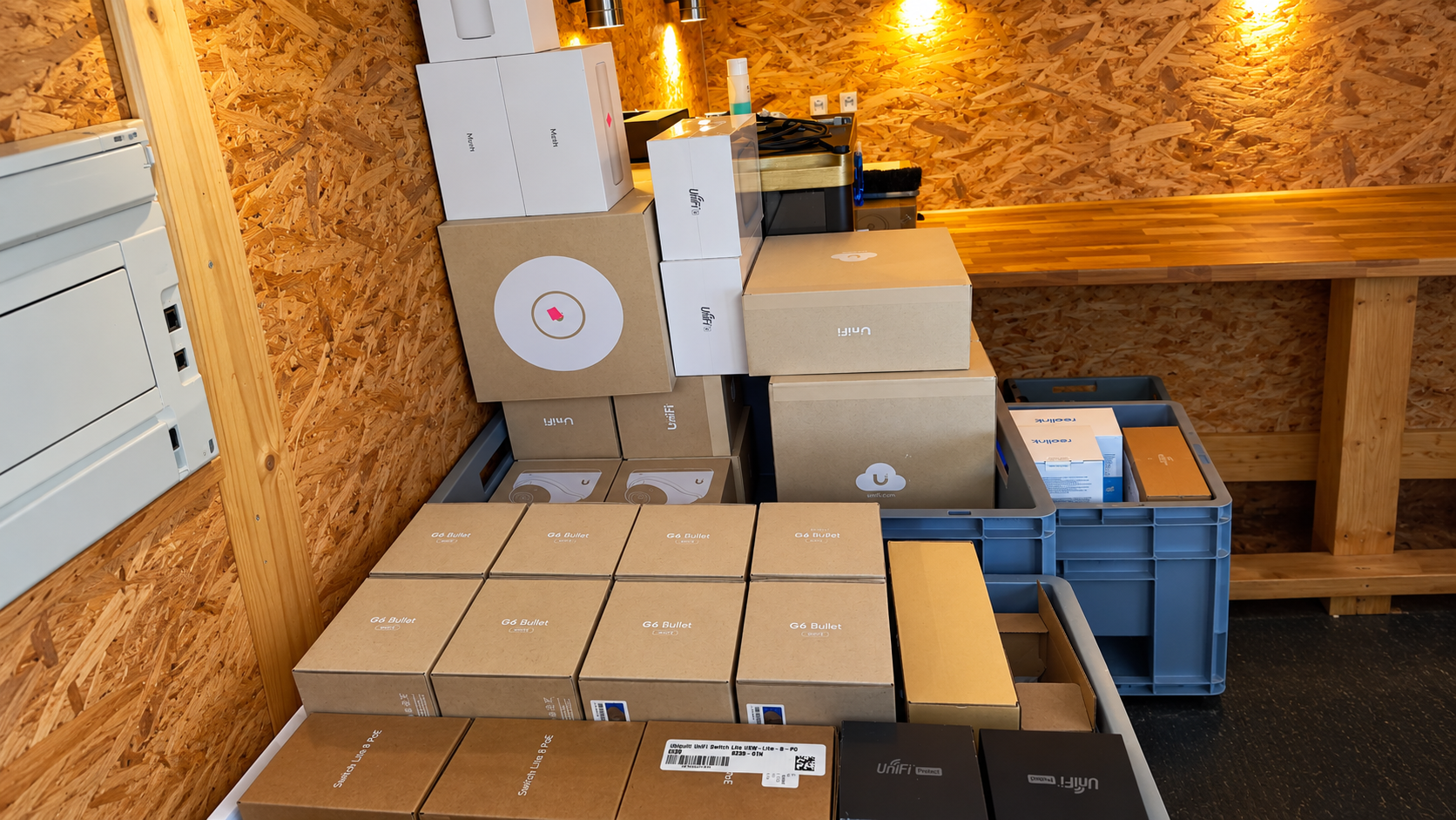 Various boxes and packages stacked in a storage area with wooden walls and a countertop.