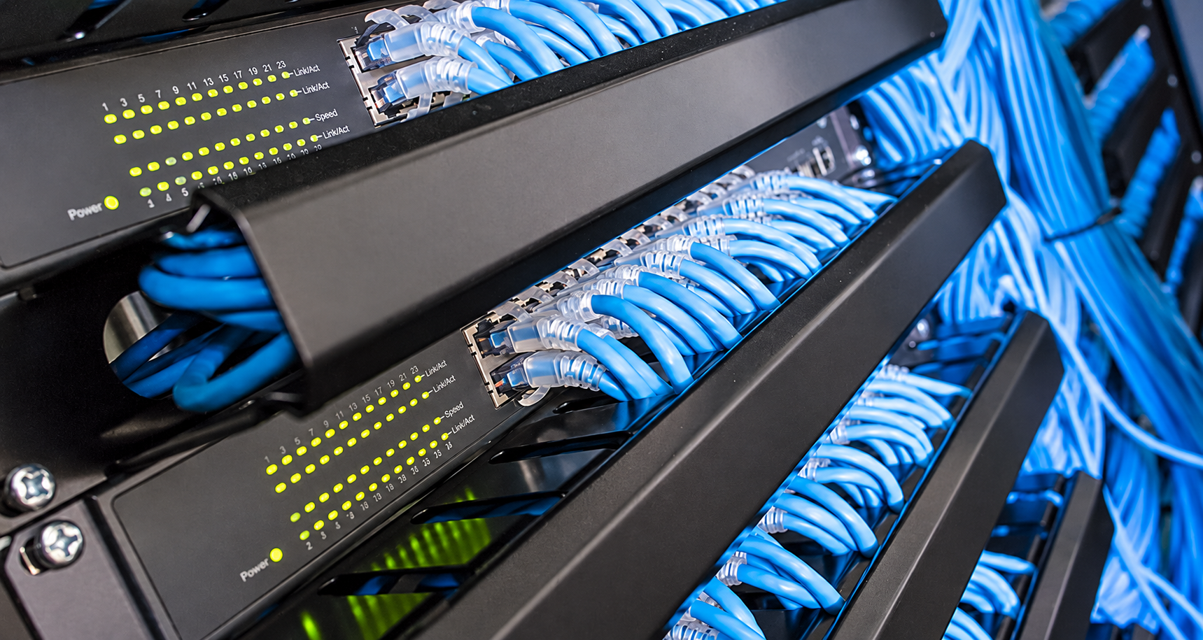 Close-up of network switches with blue Ethernet cables connected, with LED lights indicating operation status.