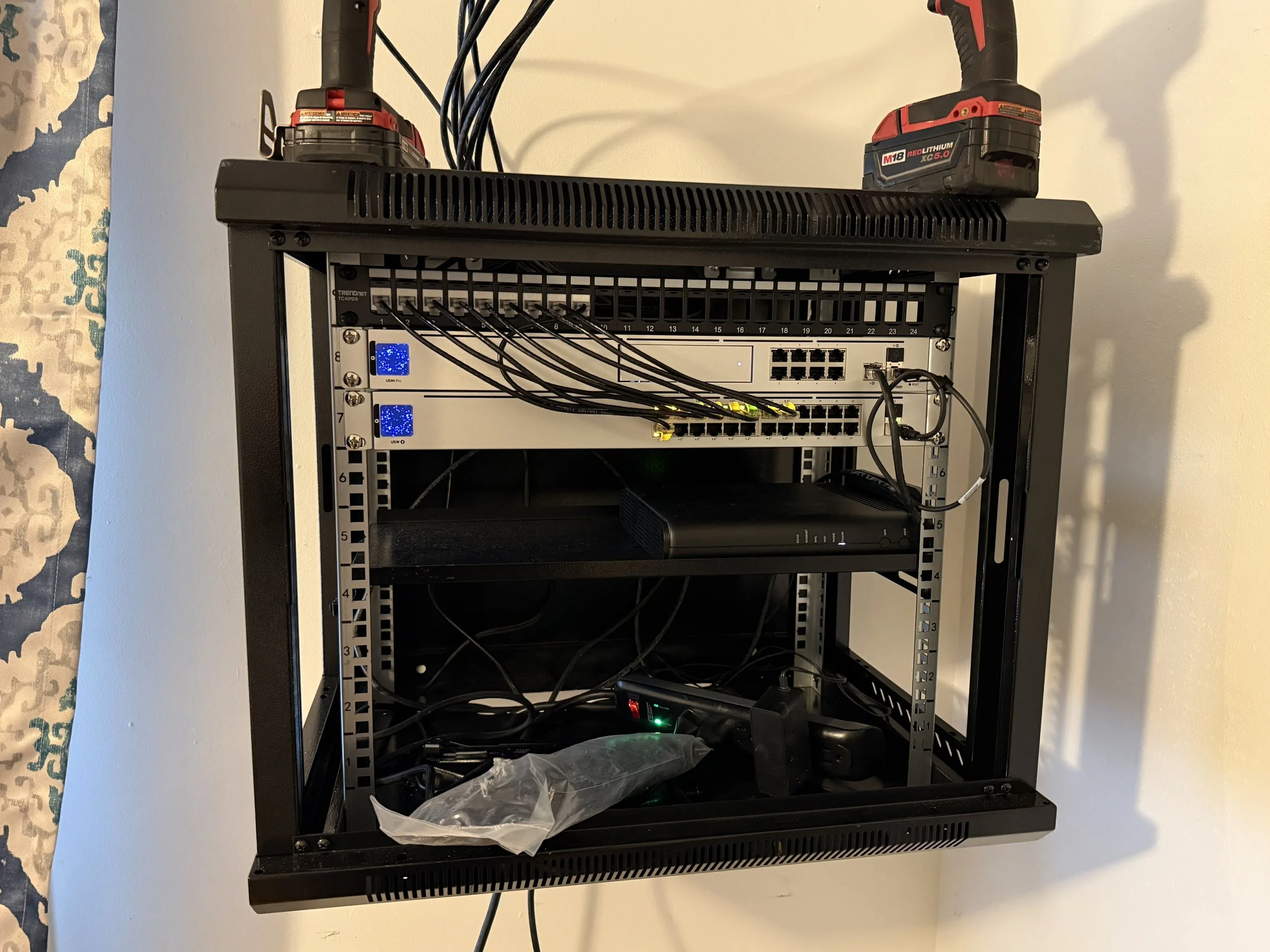 Open black server or networking rack with Ethernet switches and cables, two red and black power tools on top, against a light-colored wall.