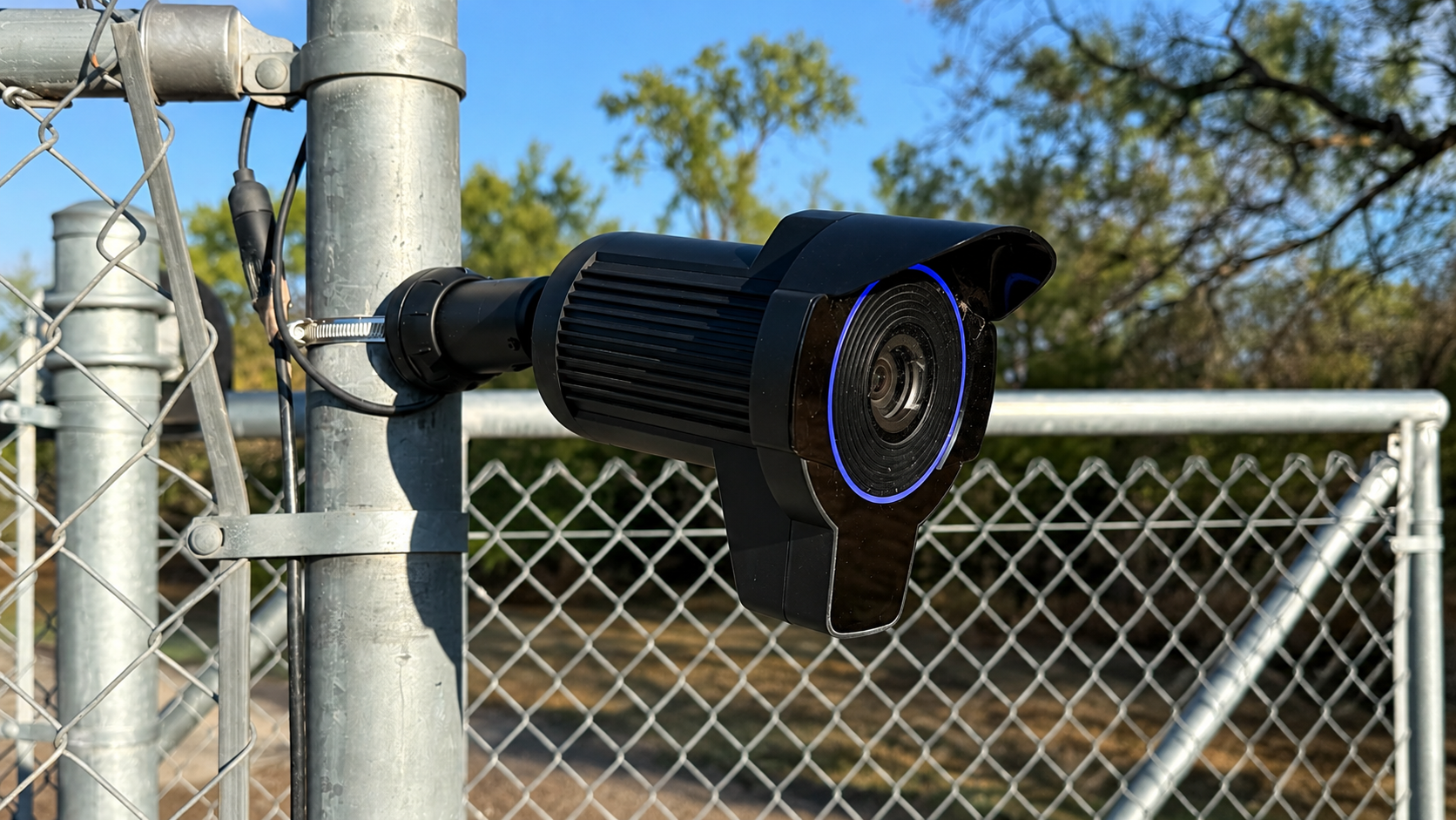 security camera mounted on a metal fence with trees in the background
