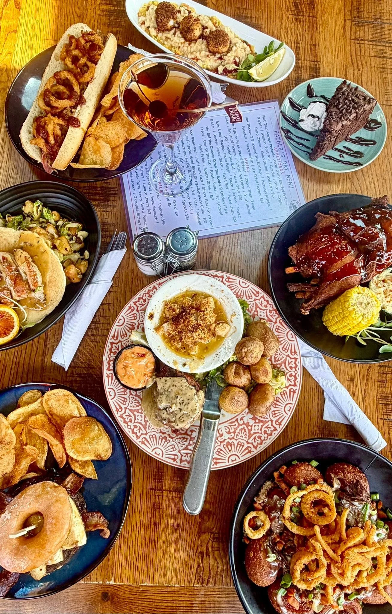 A table filled with various plates of food including sandwiches, fried appetizers, salad, a dessert ice cream cone, a bowl of pasta, and drinks in a restaurant setting.