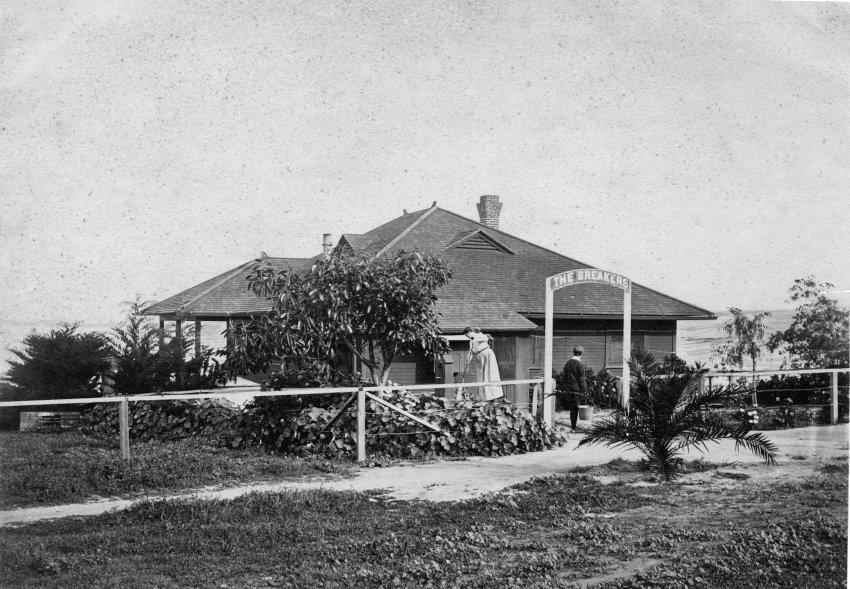 old photograph of one of La Jolla's early beach cottages. A single story home with a fence, landscaping and a view of the Pacific Ocean.