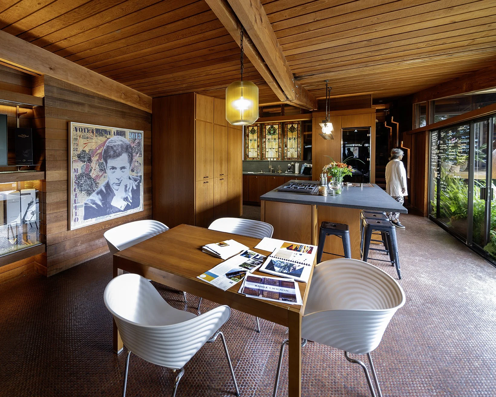 interior image of home. All wood ceiling, cabinetry and walls with a penny floor. Kitchen table and island with flowers and pendant lighting.