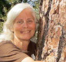 white haired woman hugging a tree in a brown shirt