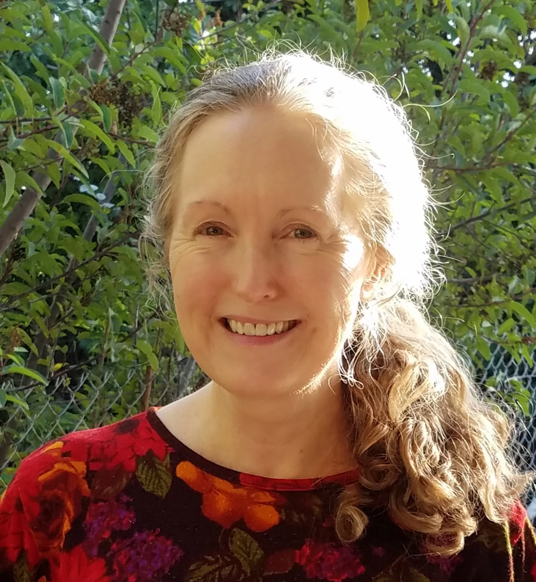 woman with ponytail smiles in front of tree