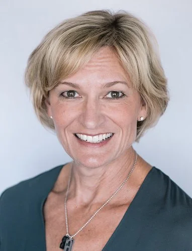 headshot of woman in grey top and pendant necklace