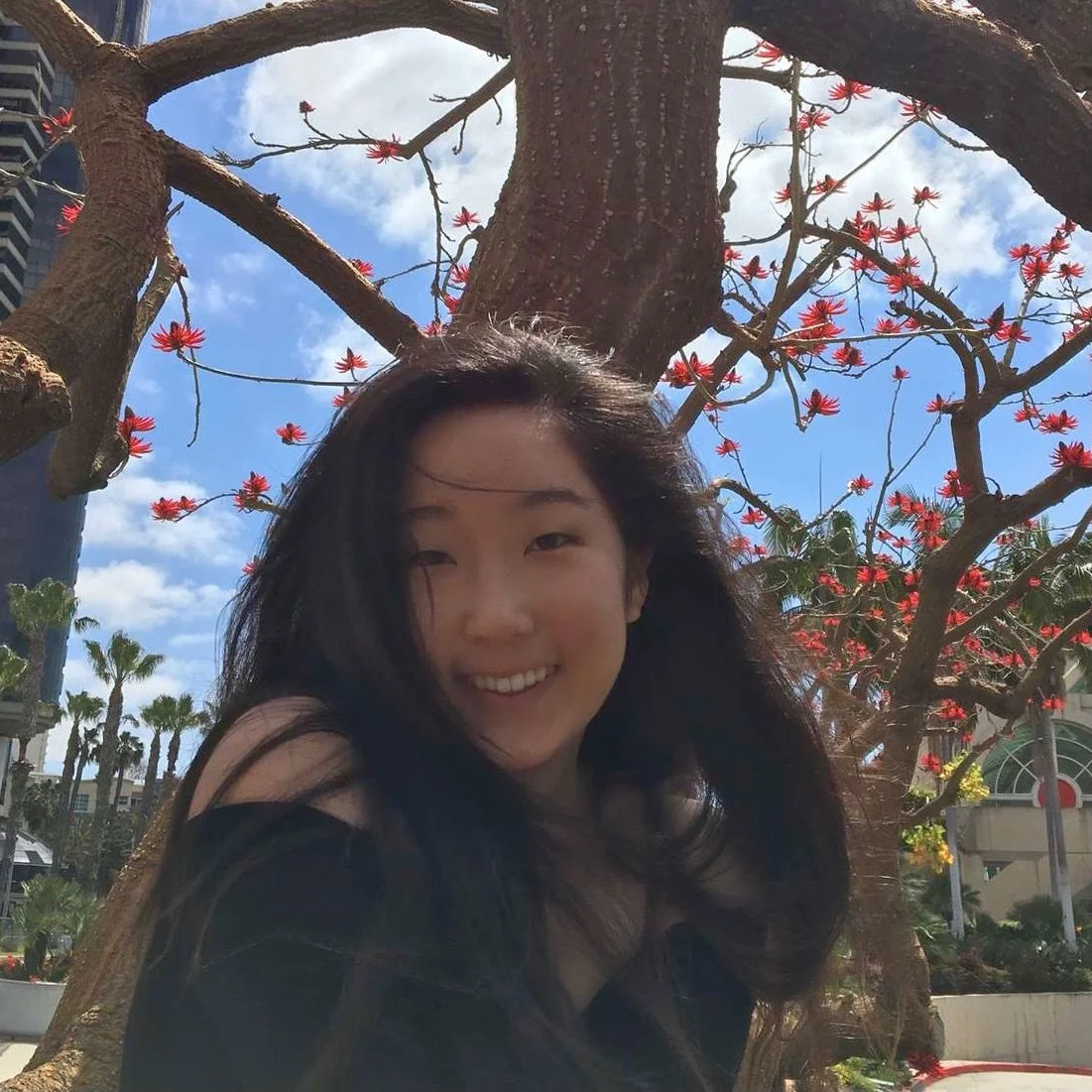young woman with long black hair in front of a tree