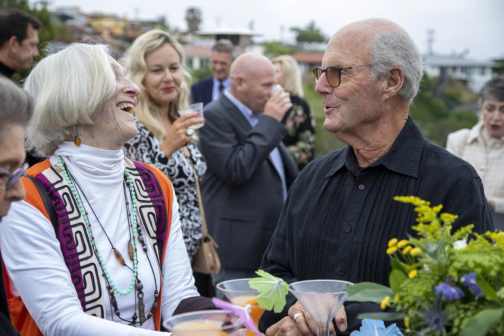 A woman with short white hair laughs with a friend opposite her.