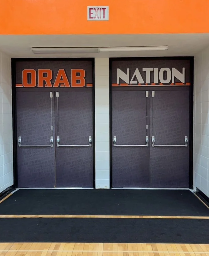Double doors with 'ORAB NATION' sign above, exit sign above, and black rug in front.