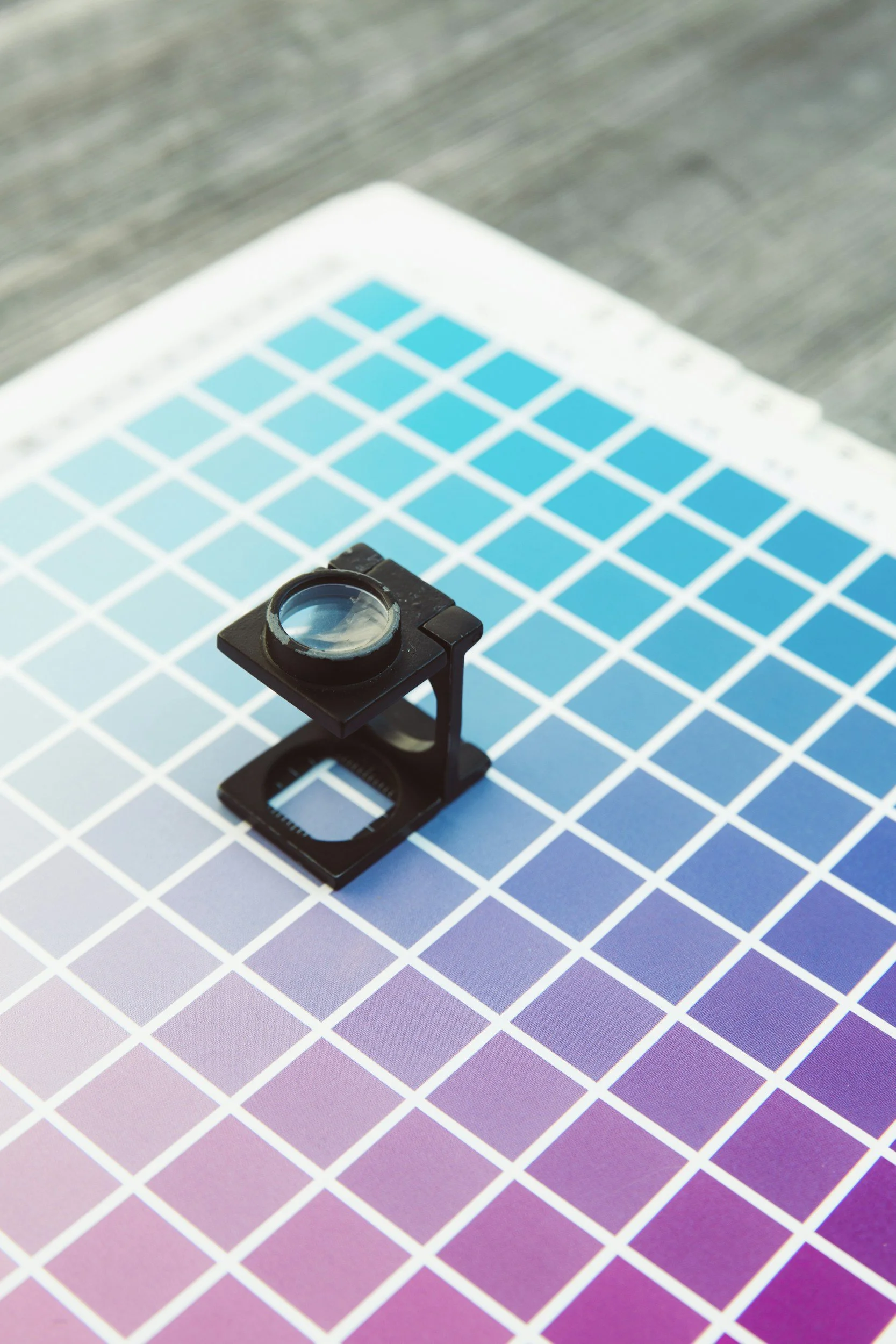 Color calibration chart with blue squares and a magnifying glass on a pastel-colored gradient background.