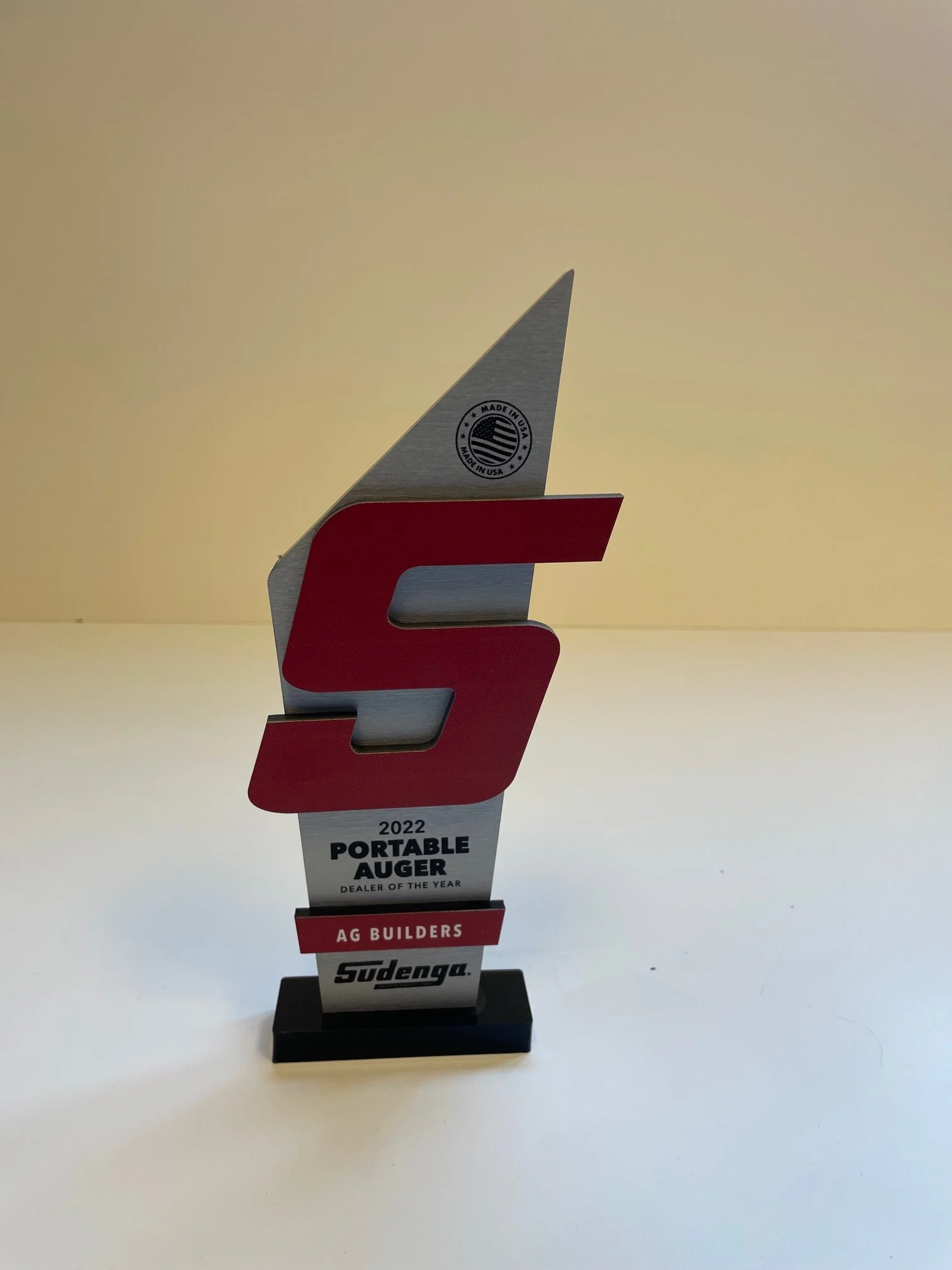 Award trophy for 2022 Portable Auger Dealer of the Year, presented by Sudenga, with a stylized red and silver design, mounted on a black base.
