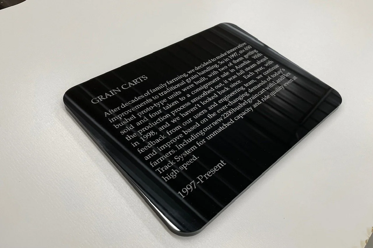 A black rectangular plaque with white engraved text about grain carts, resting on a white surface.