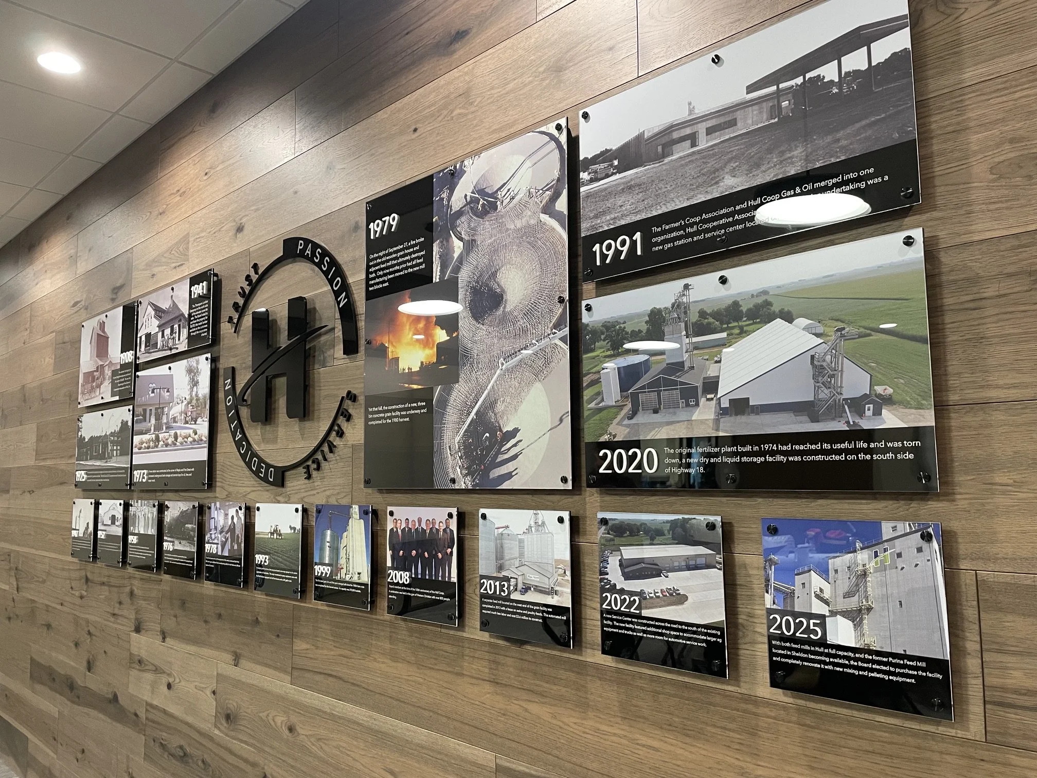 A wooden wall with a timeline display of photographs and text panels showing significant events from 1941 to 2025, including infrastructure and industrial developments.
