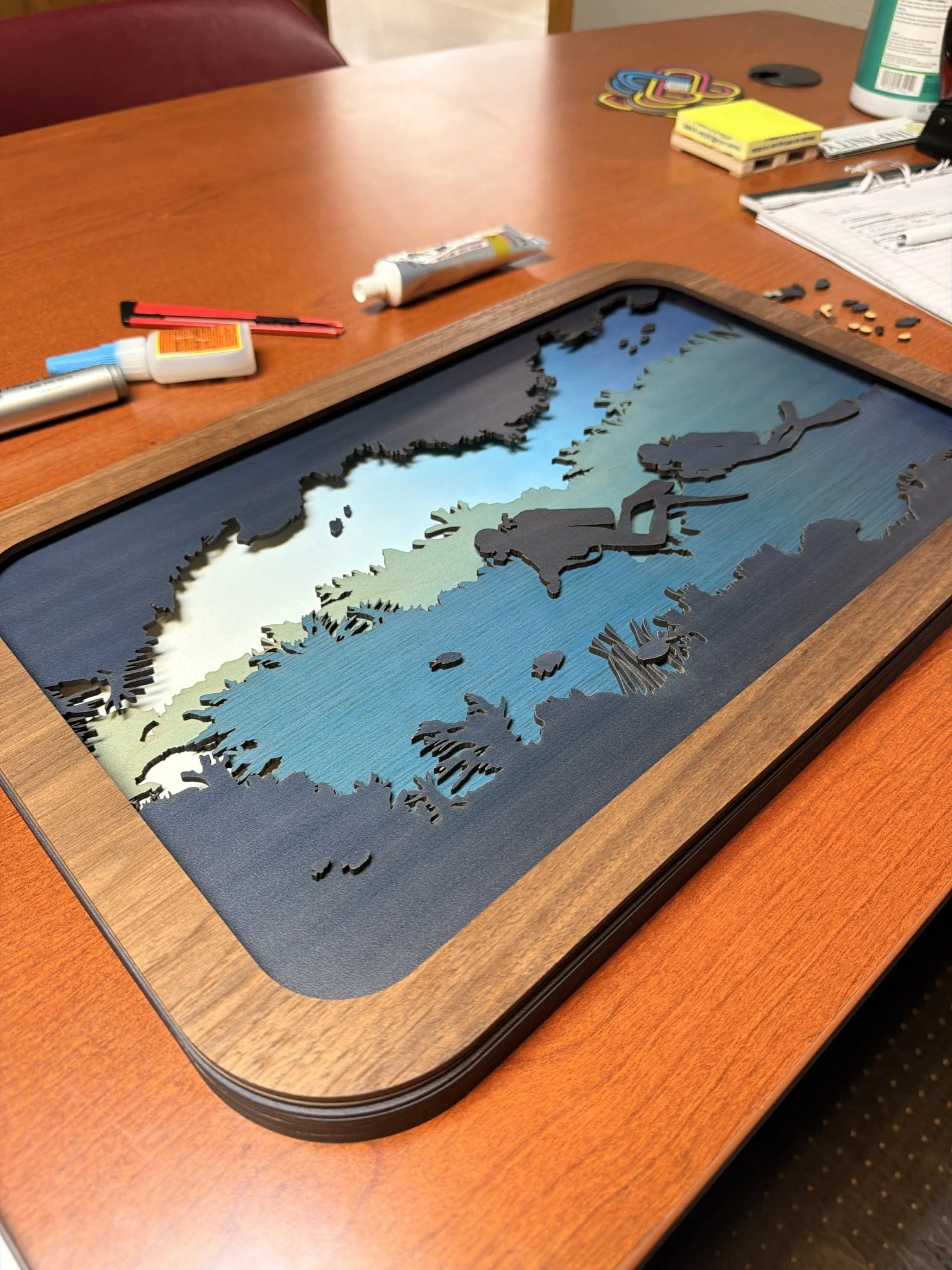 A wooden table with a decorative wooden map of Canada, a glue tube, crafting supplies, and notes.