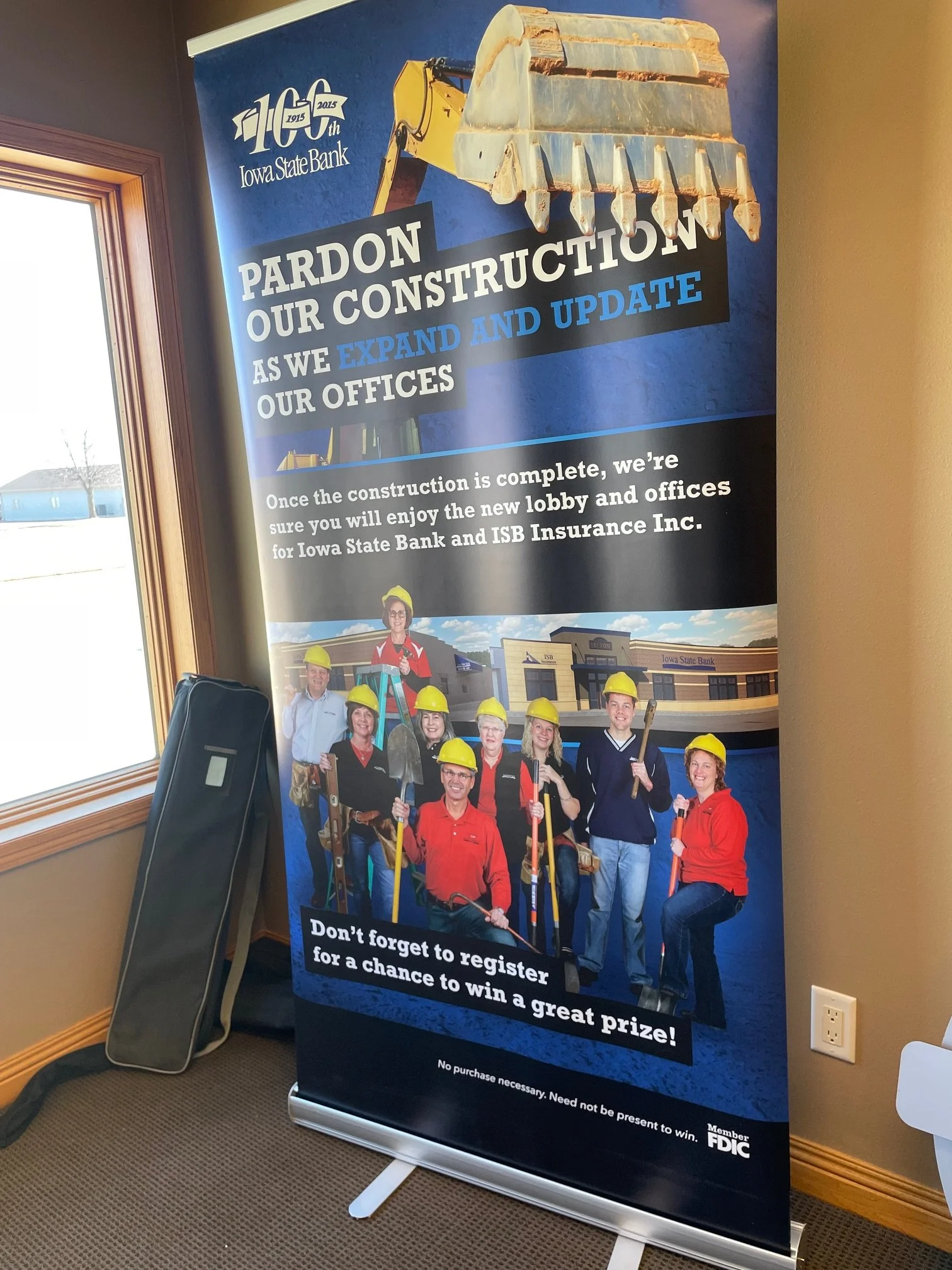 A vertical banner for Iowa State Bank celebrating its 100th anniversary with construction-themed imagery. It features a excavator bucket at the top and a group of people wearing yellow construction helmets holding tools in front of a new bank buildin