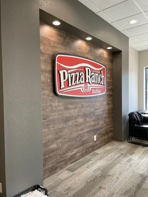 Indoor wall with a Pizza Ranch logo sign and ceiling lights