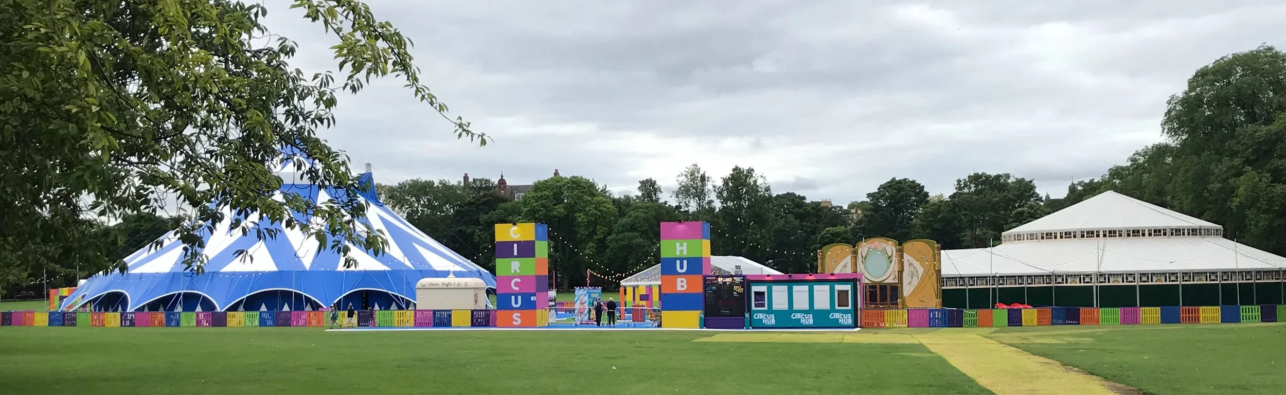 Colorful circus tents on a green grassy field with trees in the background