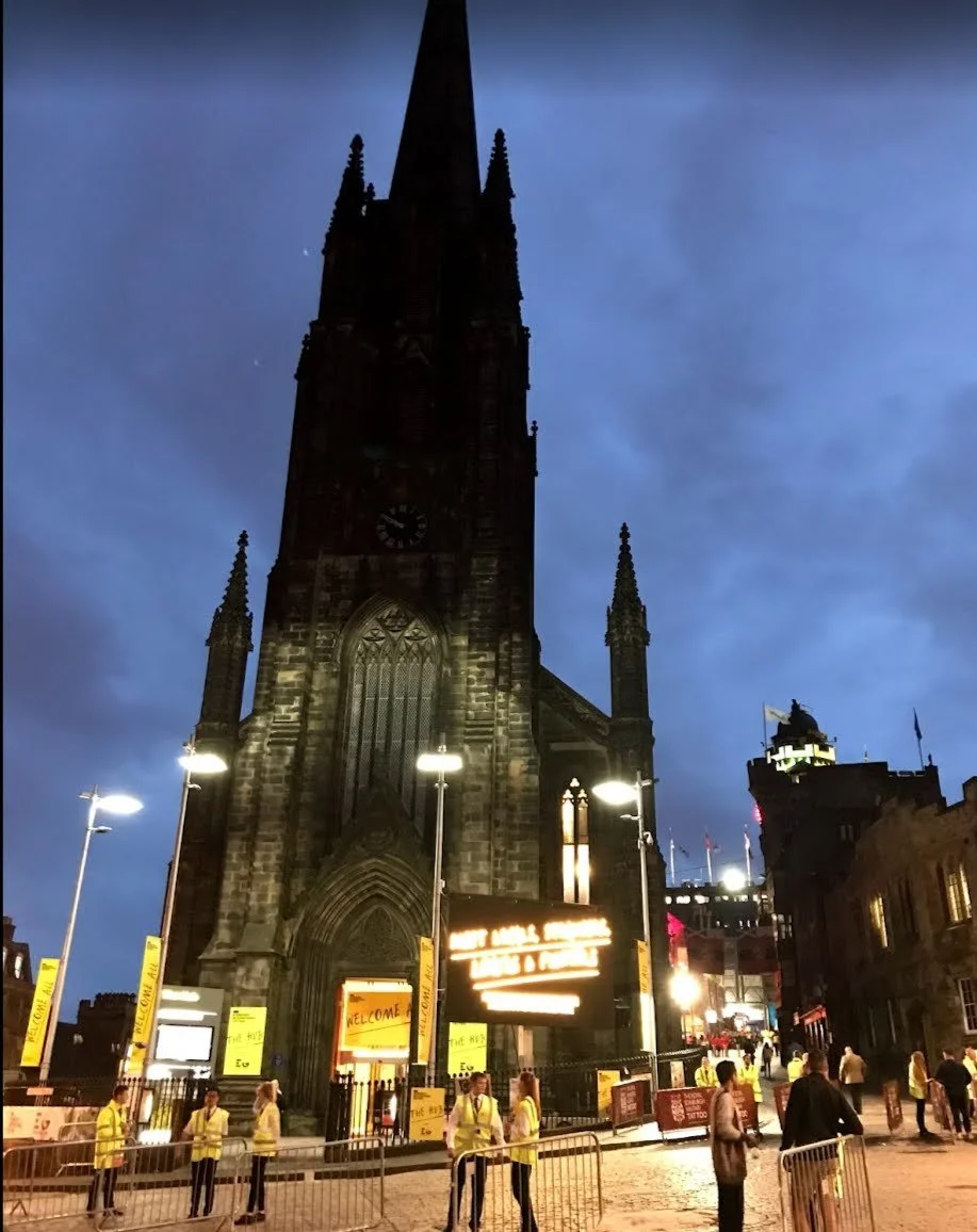 A tall gothic tower at night with yellow signs that say "The Hub"