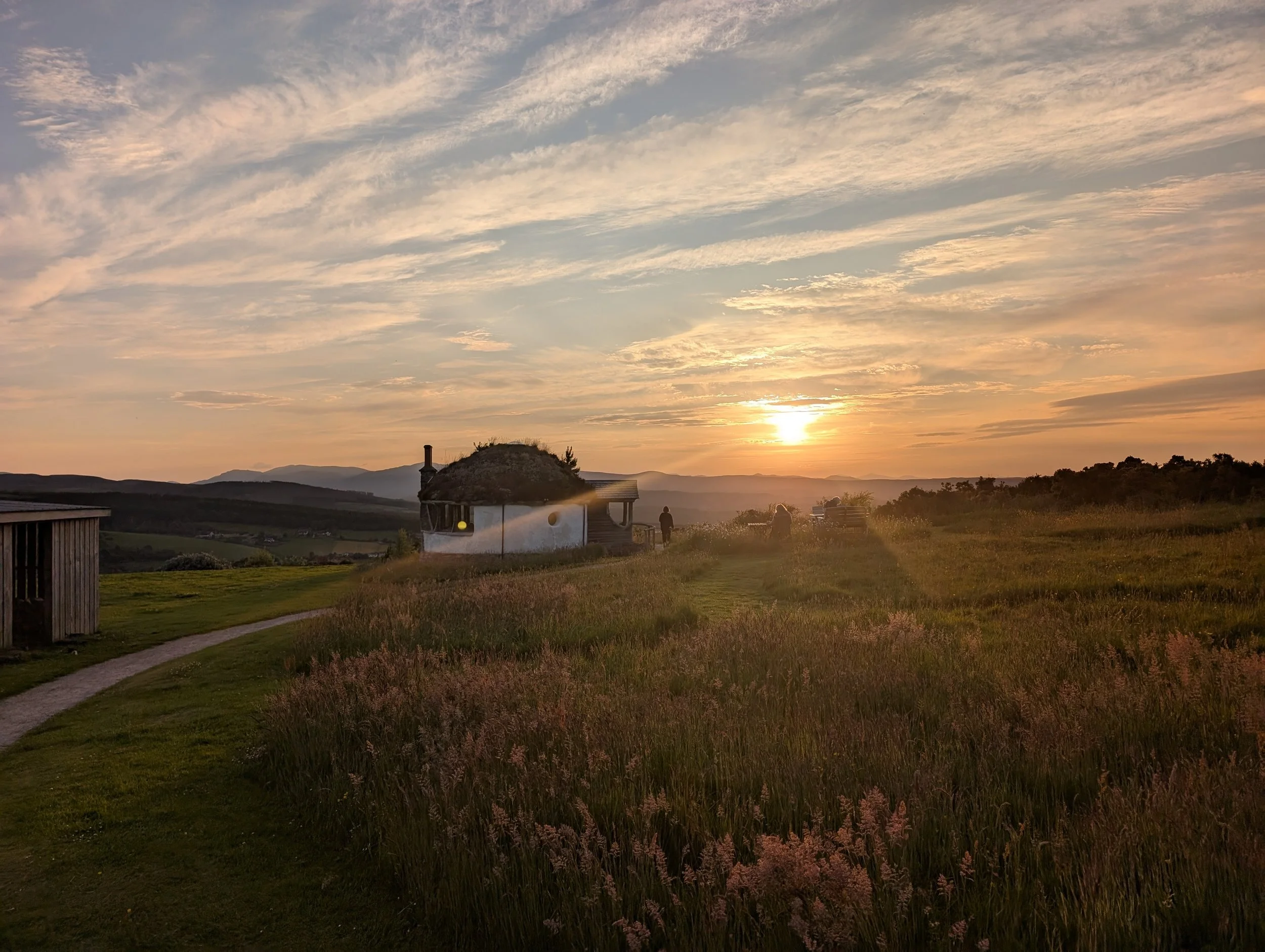 The sun setting over Scottish Highlands hills with a small hut in the foreground.