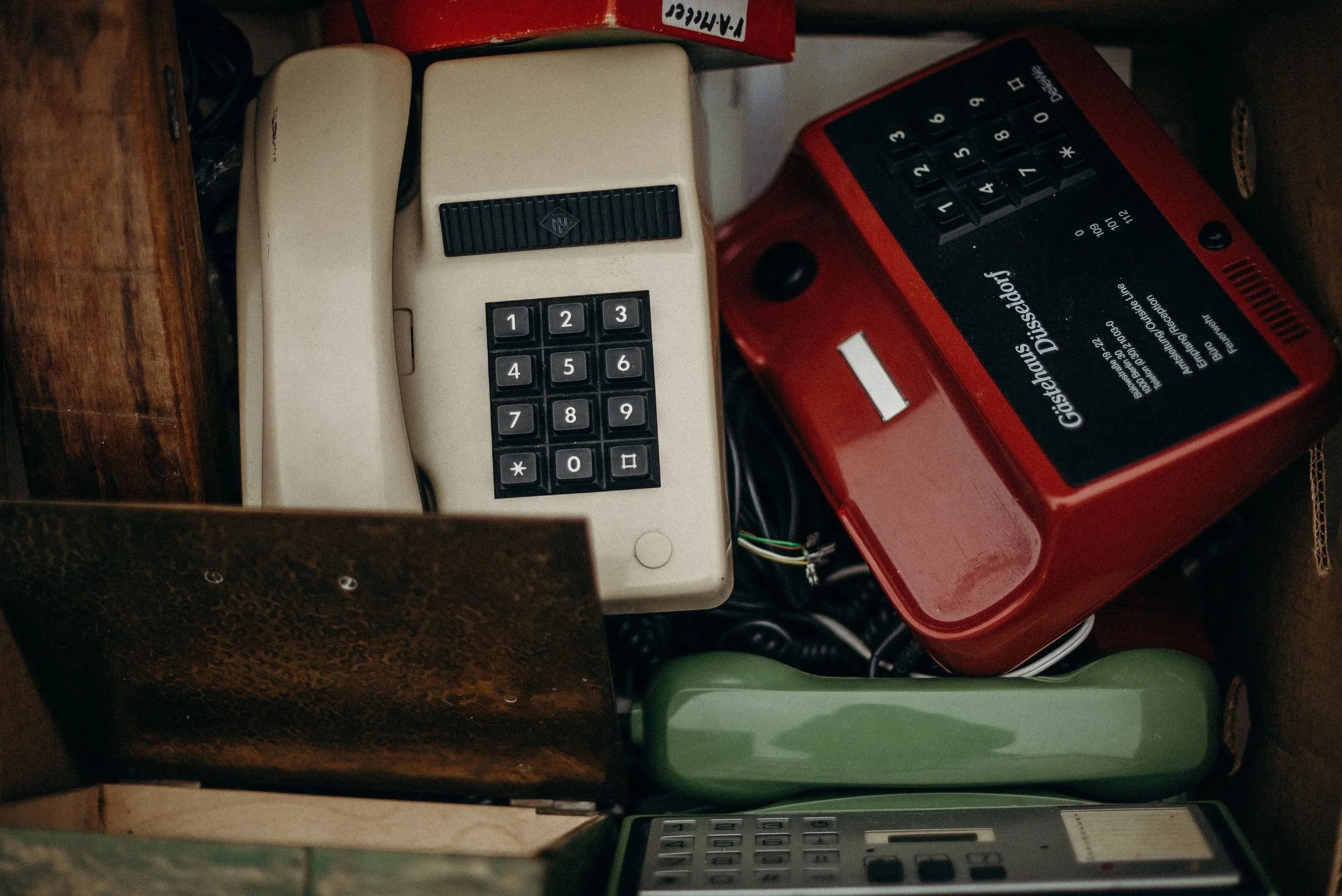 A collection of vintage objects, including an old rotary phone, a red calculator, a tape recorder, and various other electronic devices on shelves and in a storage area.