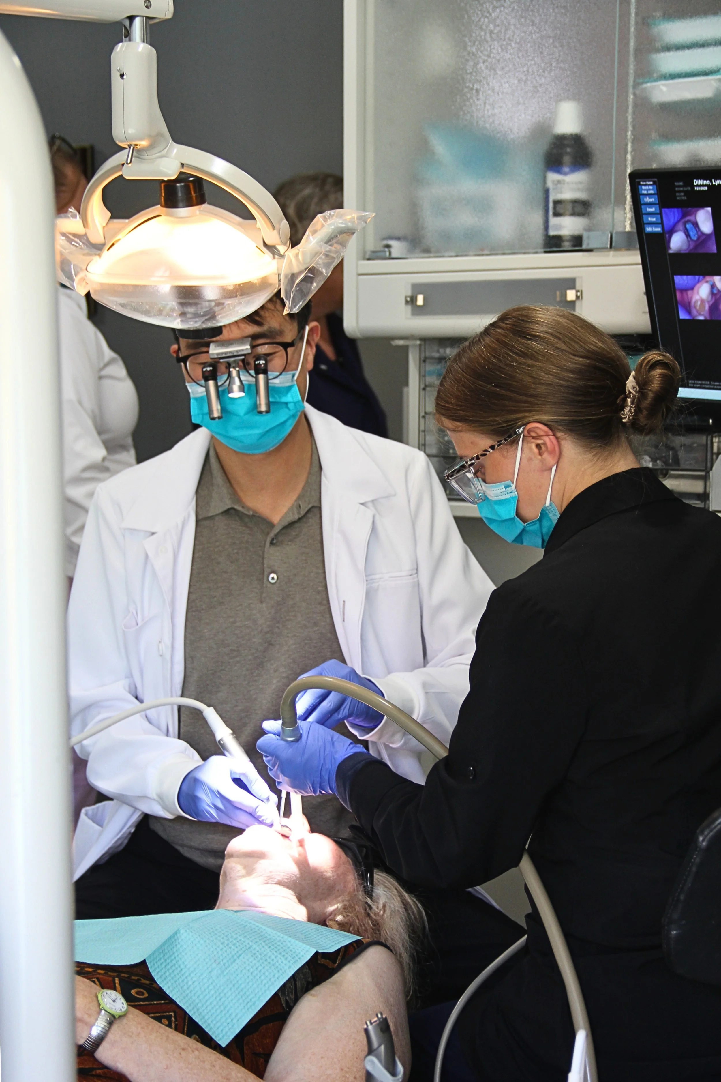Dental professionals performing a procedure on a patient in a clinic, with monitors and medical equipment present.