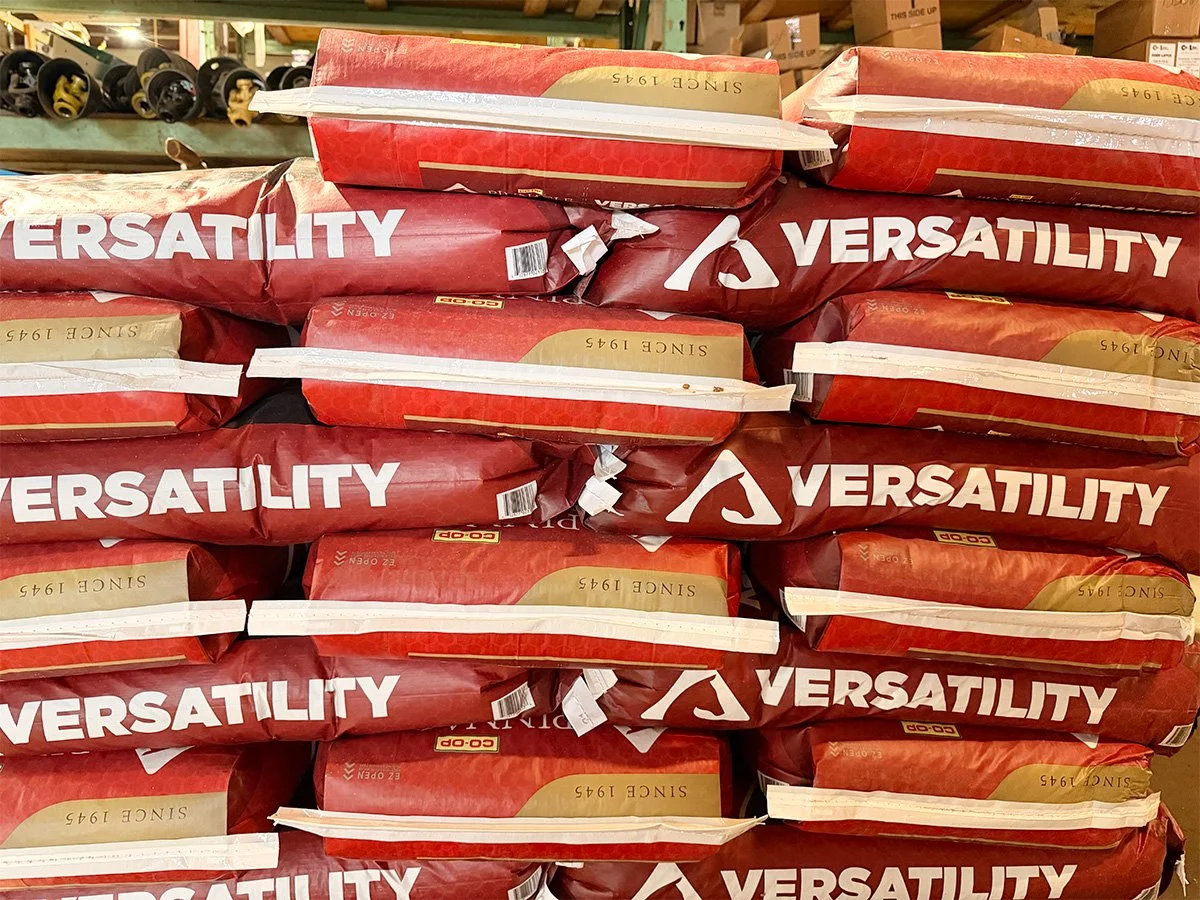 Stacks of bags of Versatility dog food in a store aisle.