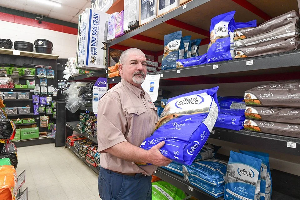 A man shopping for pet food on store shelves, holding a large bag of Nutri Source brand dog food.