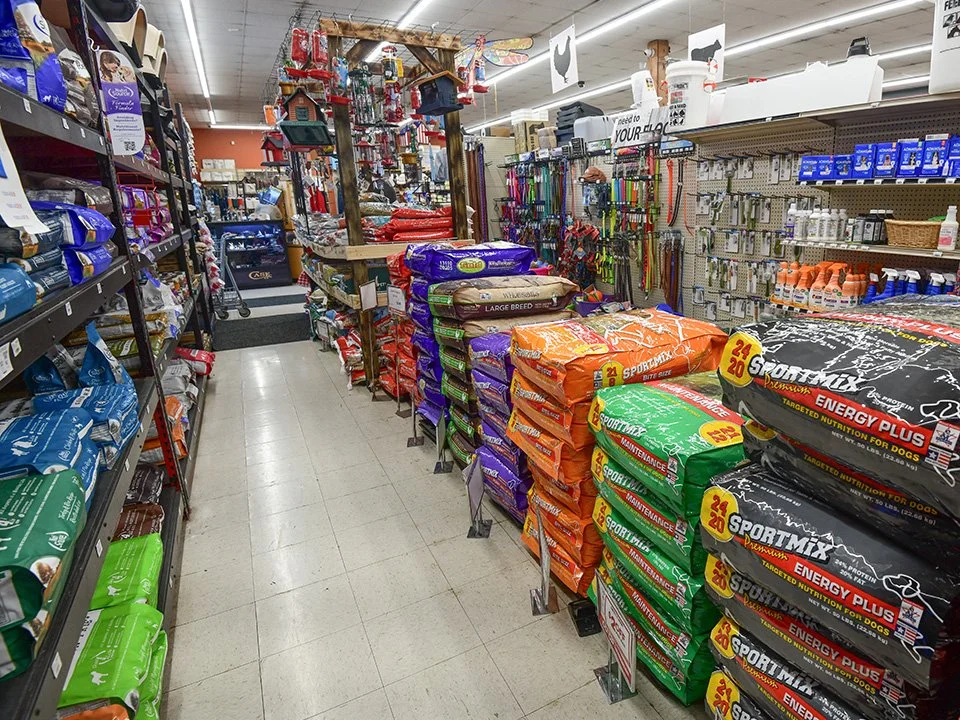 Aisle in a pet store with shelves stocked with pet food bags, supplies, and accessories.