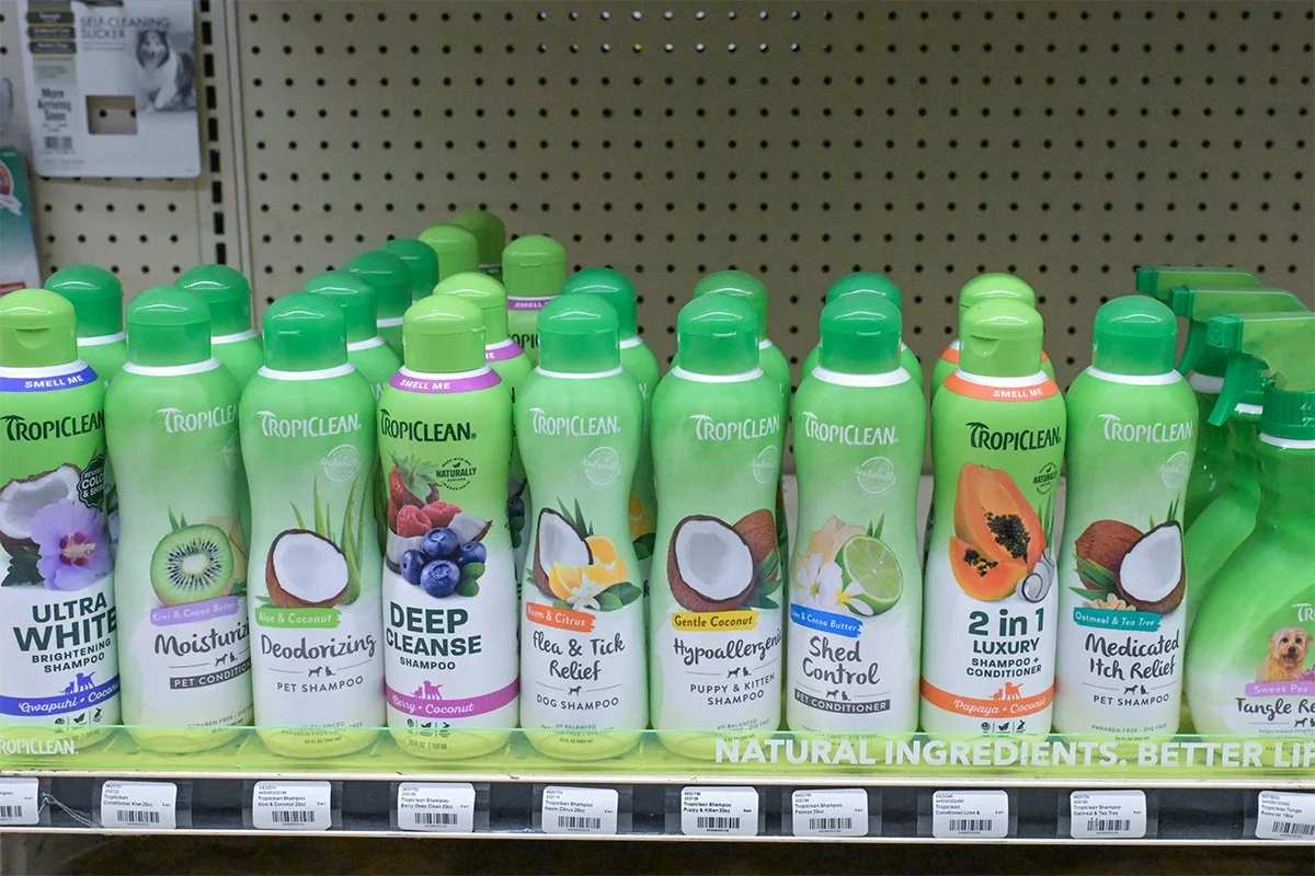 A collection of Tropiclean pet shampoo bottles on store shelf, with various scents like Deep Clean, Flea & Tick Relief, Hypoallergenic, and 2-in-1 Luxury, all in green packaging.