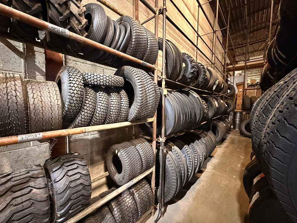 A storage area with multiple shelves holding tires of various sizes and treads, arranged horizontally and vertically, with some stacked and others lined up.