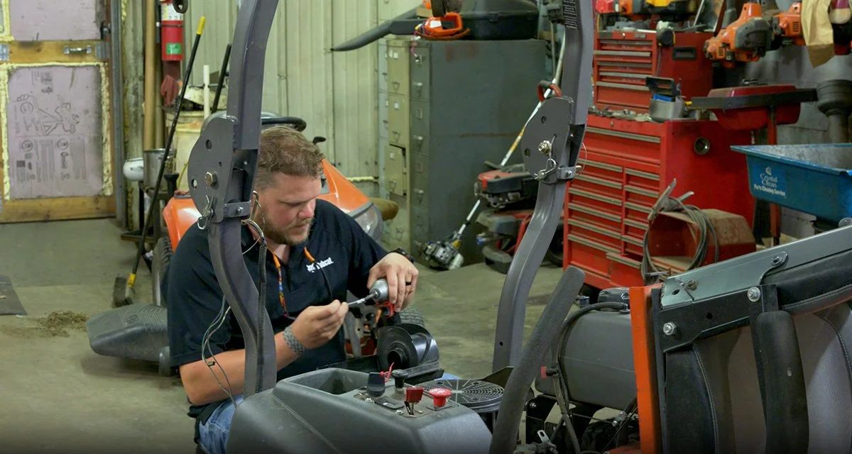 A man working on a machine in a cluttered workshop with tools and equipment.