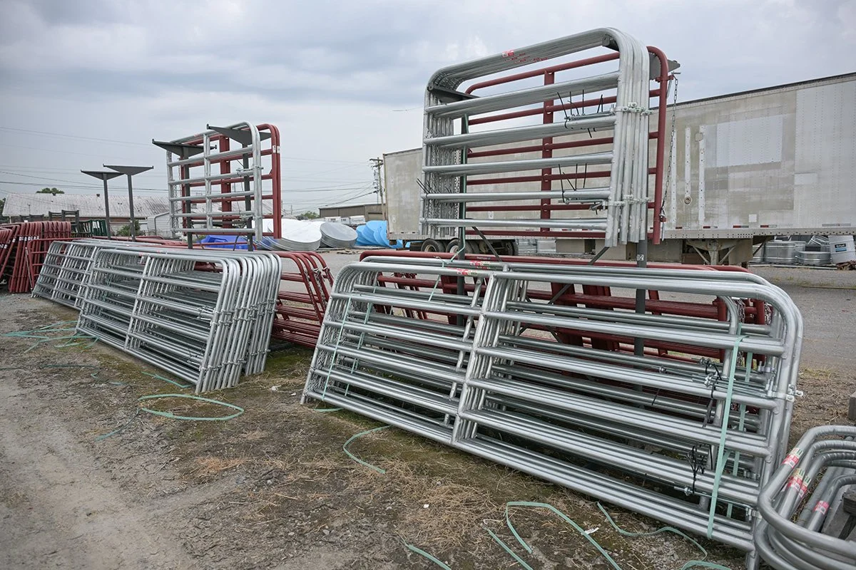 Metal frame structures stacked outdoors in a lot, with some red and some silver-colored frames, under a cloudy sky.
