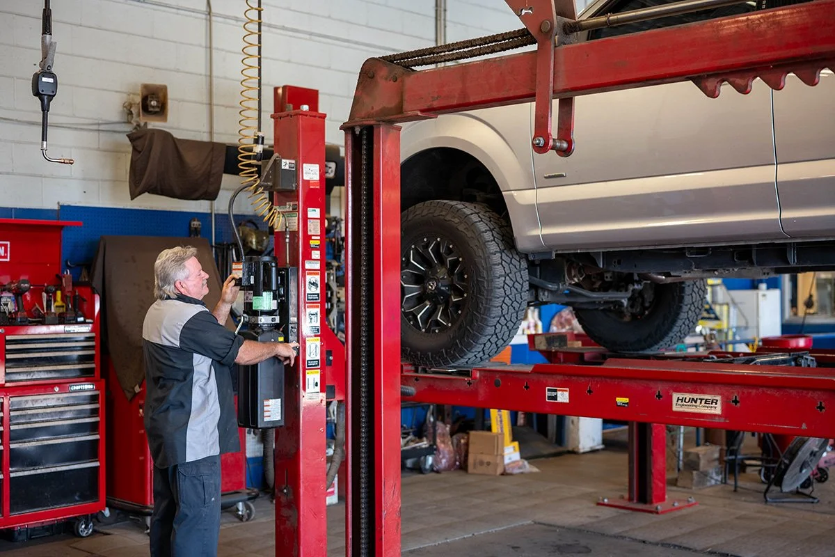 A mechanic working on a vehicle elevated on a red hydraulic lift inside an auto repair shop.
