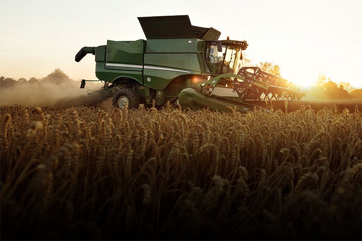 A large green combine harvester working in a wheat field at sunset.