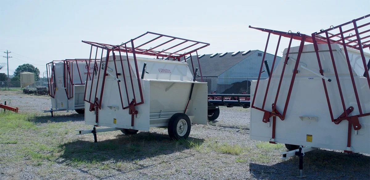 Several white utility trailers with red frames, parked outdoors on a gravel lot.