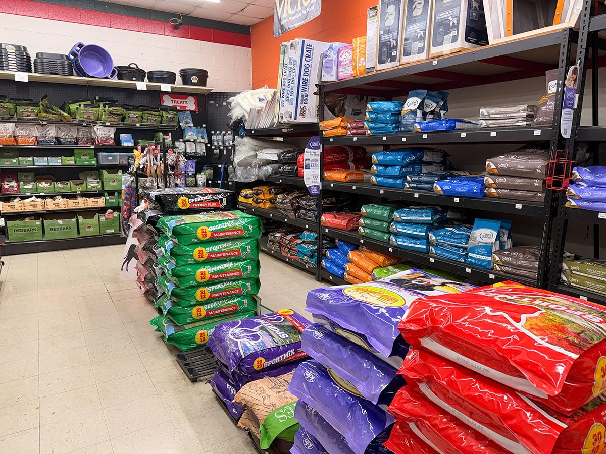 Pet store aisle with bags of pet food on shelves and containers of supplies on the wall.