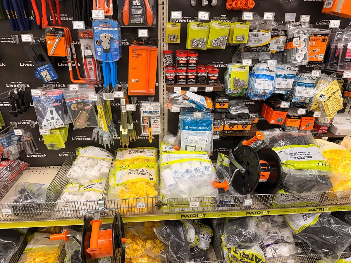 A store shelf displaying various hardware tools and supplies, including wire cutters, clamps, fasteners, wire spools, and other hardware items.