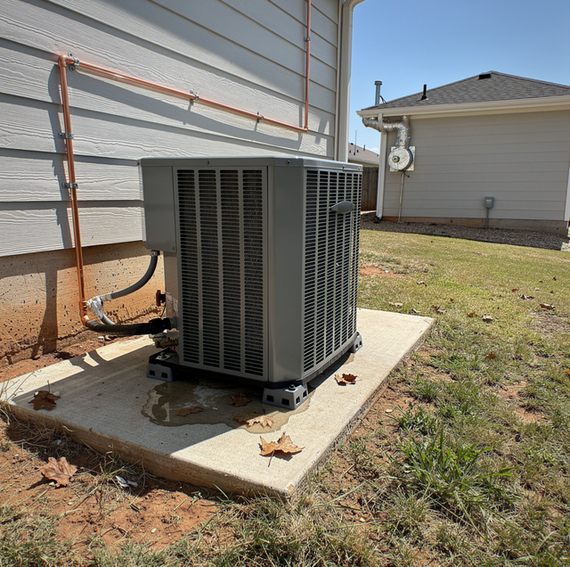 An outdoor air conditioning unit sits on a concrete pad next to a residential building with metal siding.