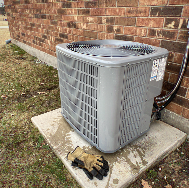 Outdoor AC condenser unit with humming compressor beside house wall