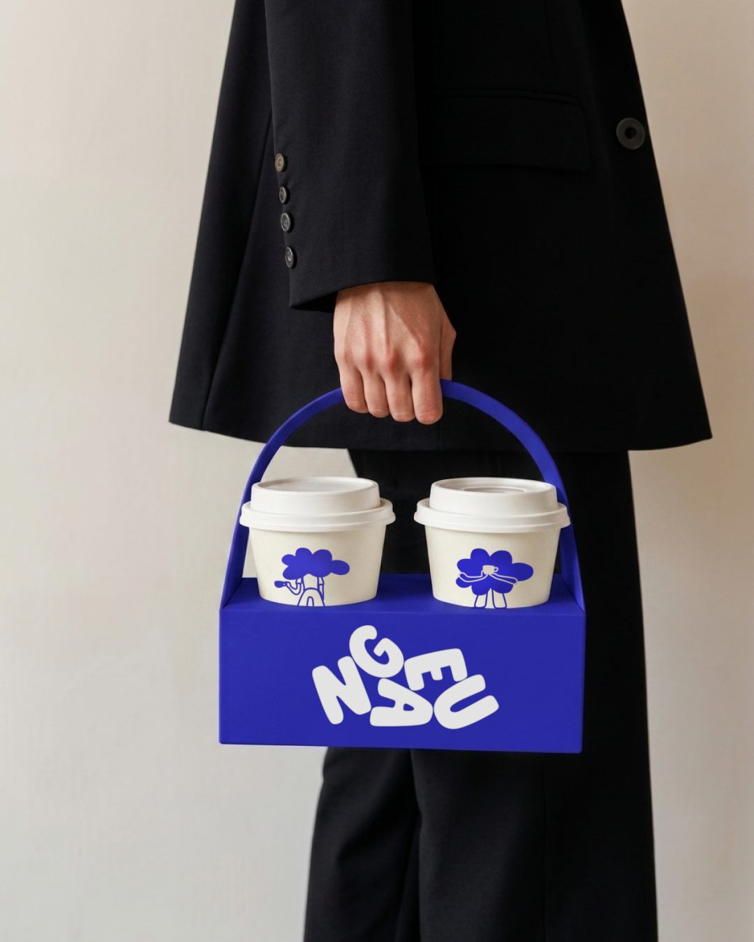 Personne en costume noir portant un porte-gobelet bleu électrique avec deux tasses à café à emporter au design graphique moderne.