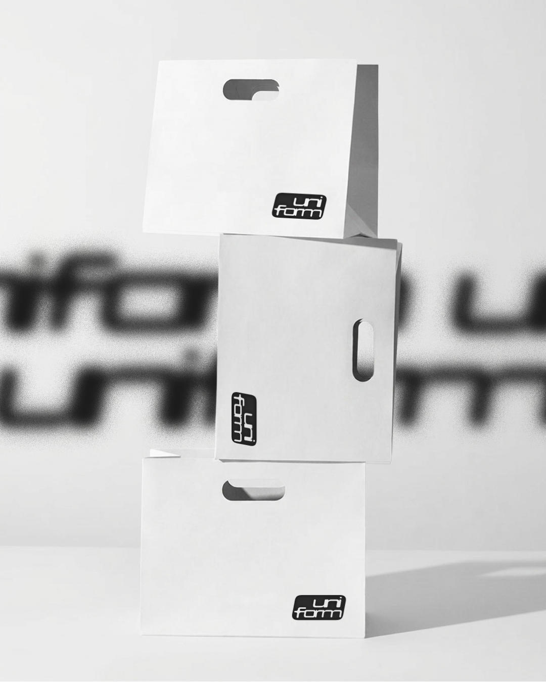 Trois cartons blancs empilés, portant le logo 'uniform' en noir, dans un espace lumineux, avec un fond flou