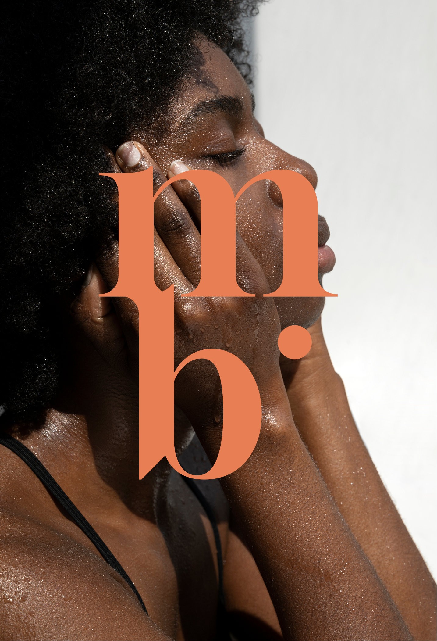 Une femme noire aux cheveux bouclés ferme les yeux, dégage la peau de son visage avec ses mains. La peau de son visage et de son corps est humide ou couverte de petites gouttelettes.